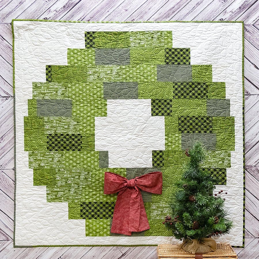 Evergreen wreath quilt displayed with Christmas greenery and red berries