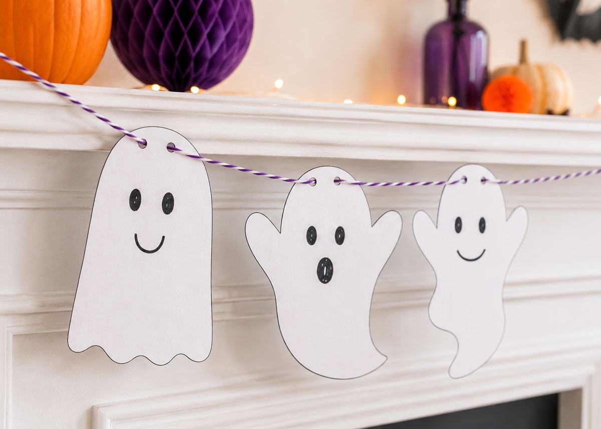 Large printable Halloween ghosts hanging from a mantel with orange and purple Halloween decorations