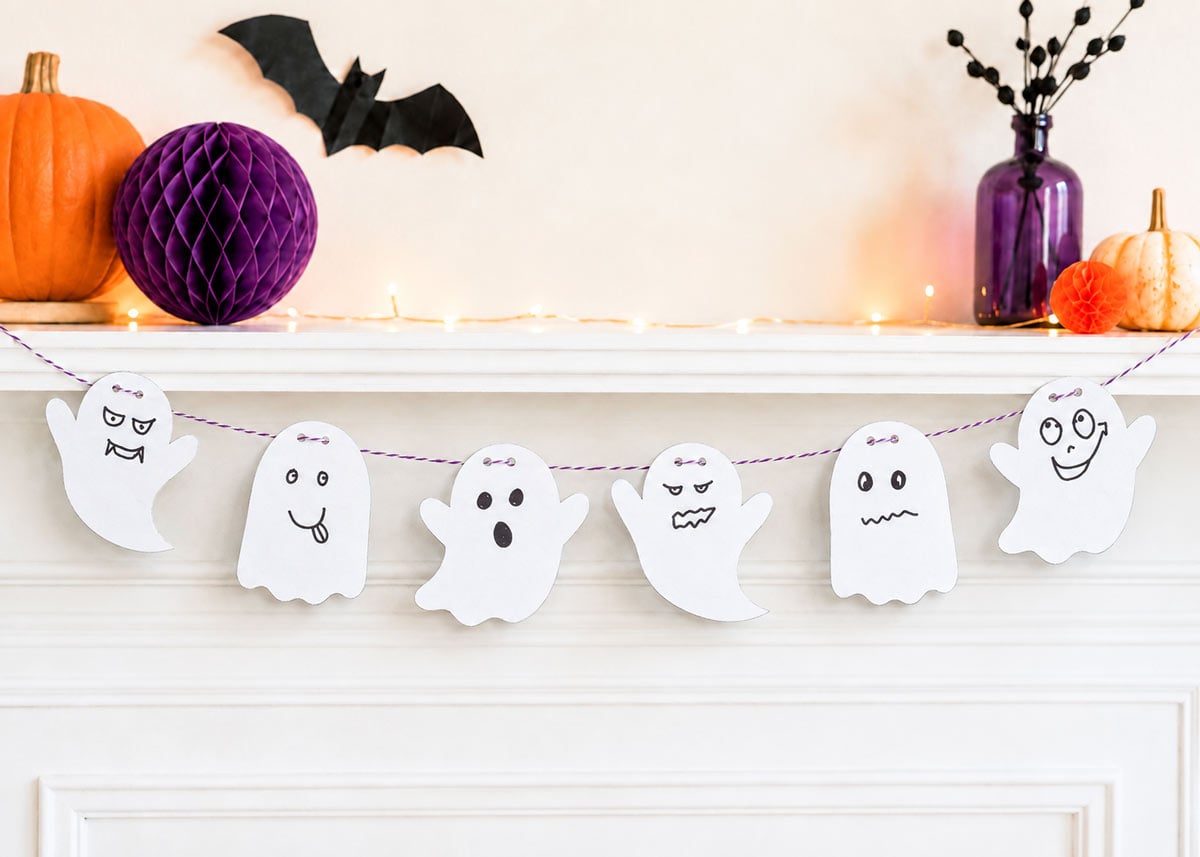 Large printable Halloween ghosts hanging from a mantel with orange and purple Halloween decorations